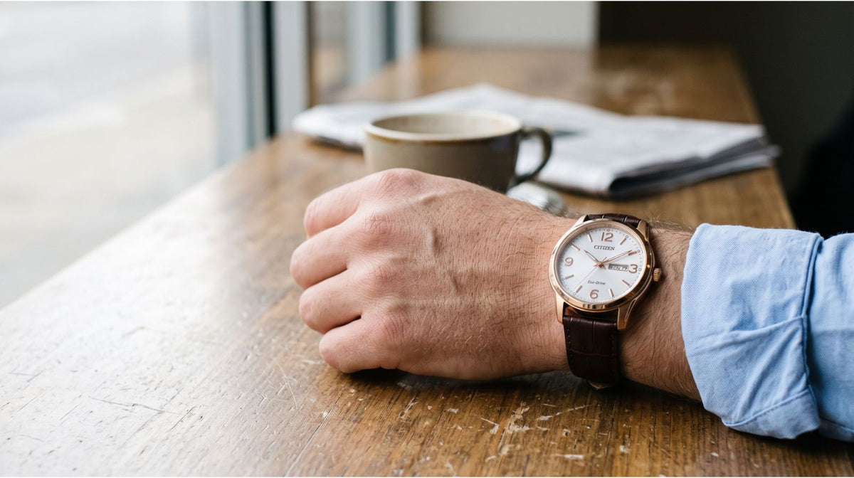 Citizen Eco-Drive med vit urtavla och brunt läderarmband på handleden hos en man vid ett fönster